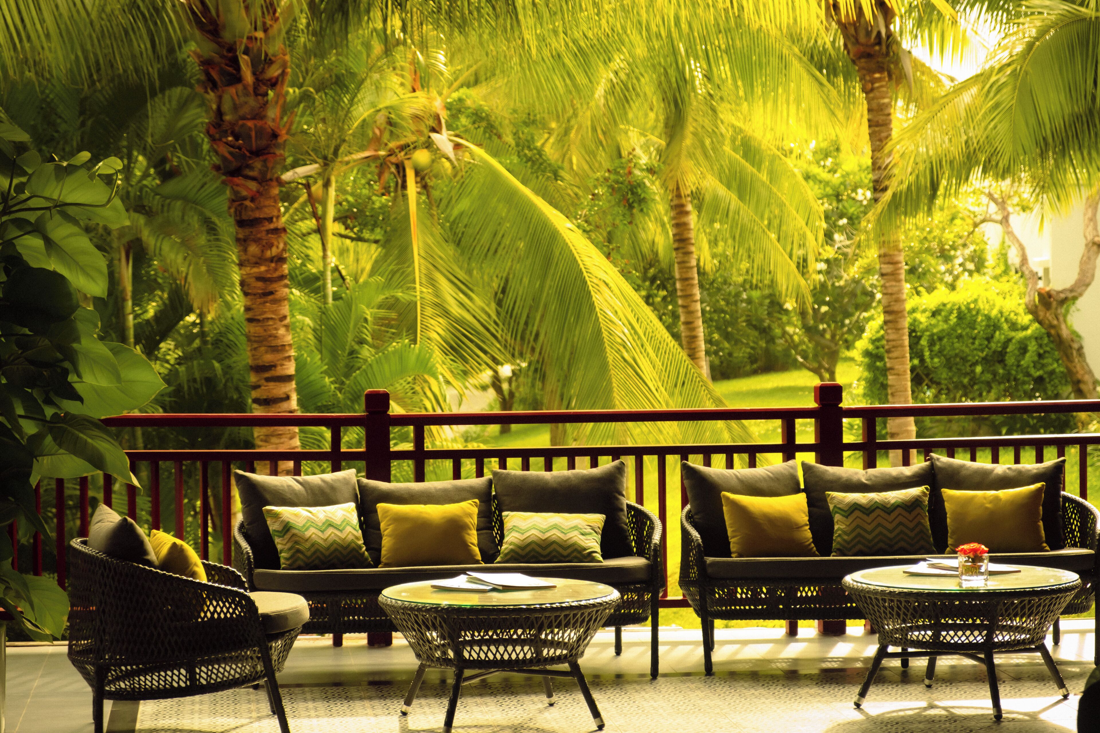 A tropical outdoor seating area with wicker furniture, a small round table, and a railing.