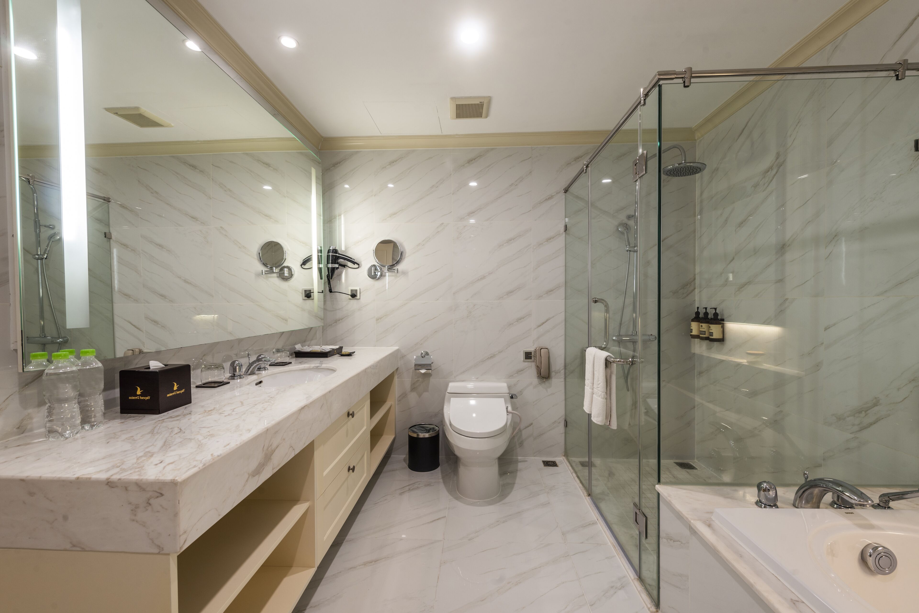 Un baño moderno con encimera de mármol, inodoro, ducha con mampara de vidrio y un espejo grande.