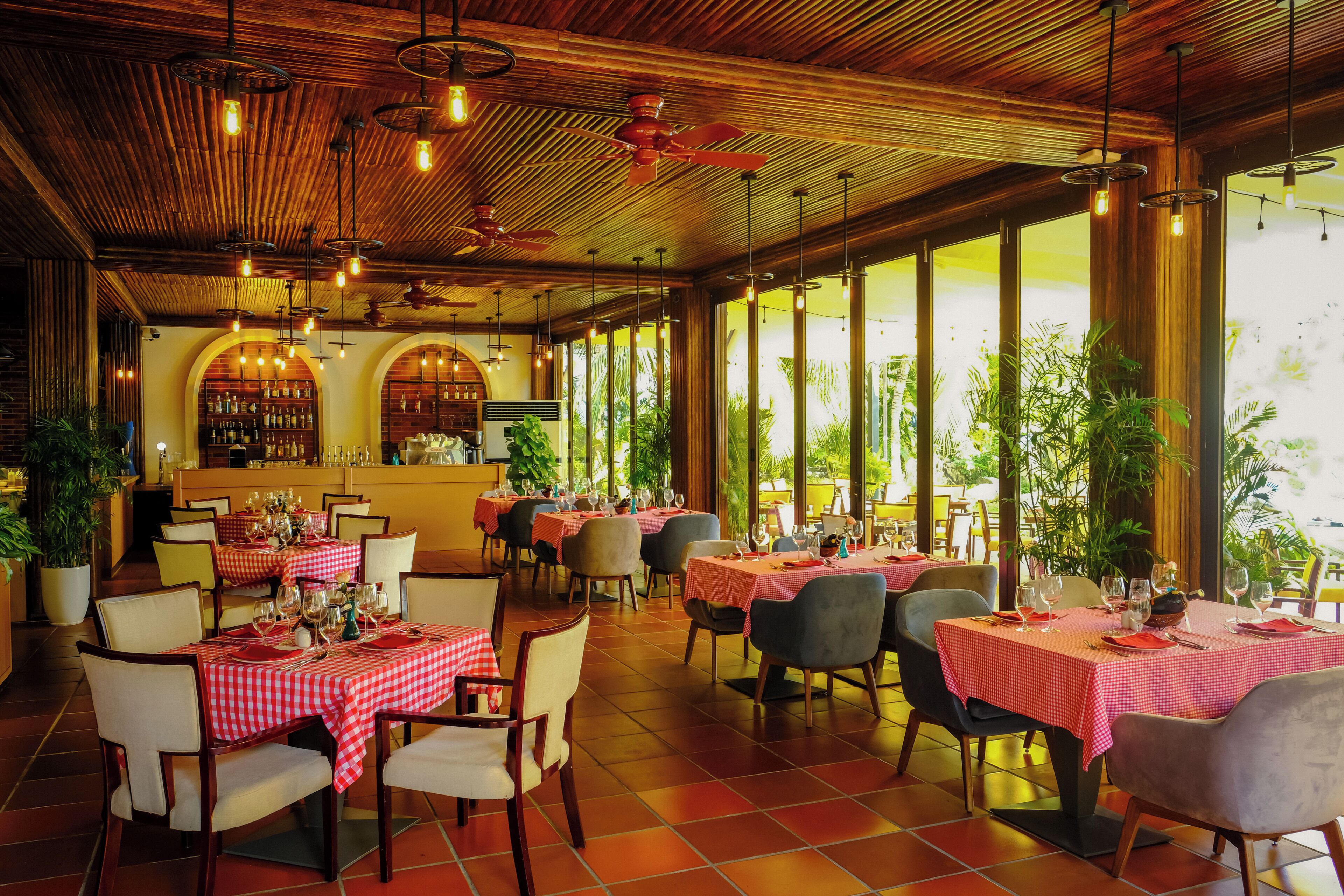 A restaurant with red and white checkered tablecloths, wooden ceiling, and large windows with plants.