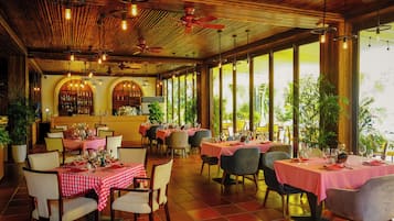 A restaurant with red and white checkered tablecloths, wooden ceiling, and large windows with plants.