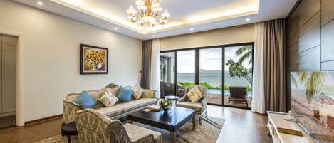 A modern living room with a sofa, armchairs, a coffee table, and a large window with a view of the ocean.
