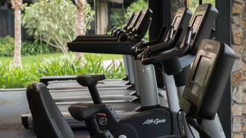 A row of stationary bikes labeled "Life Cycle" in a covered area with a view of greenery and a stone wall.