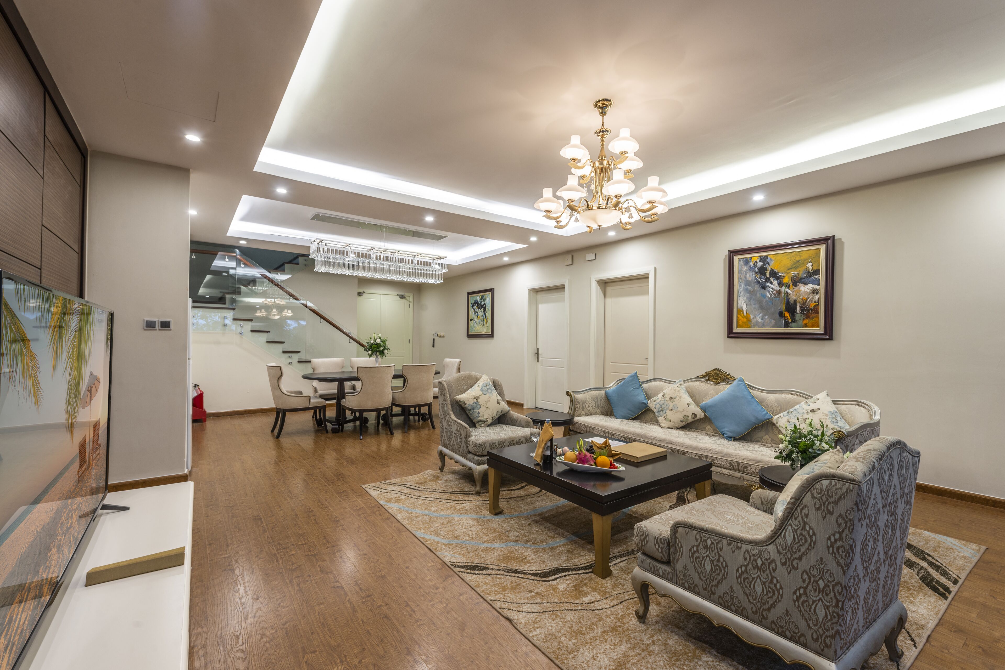 A modern living room with a sofa set, coffee table, and a chandelier. There is a staircase leading to an upper level.