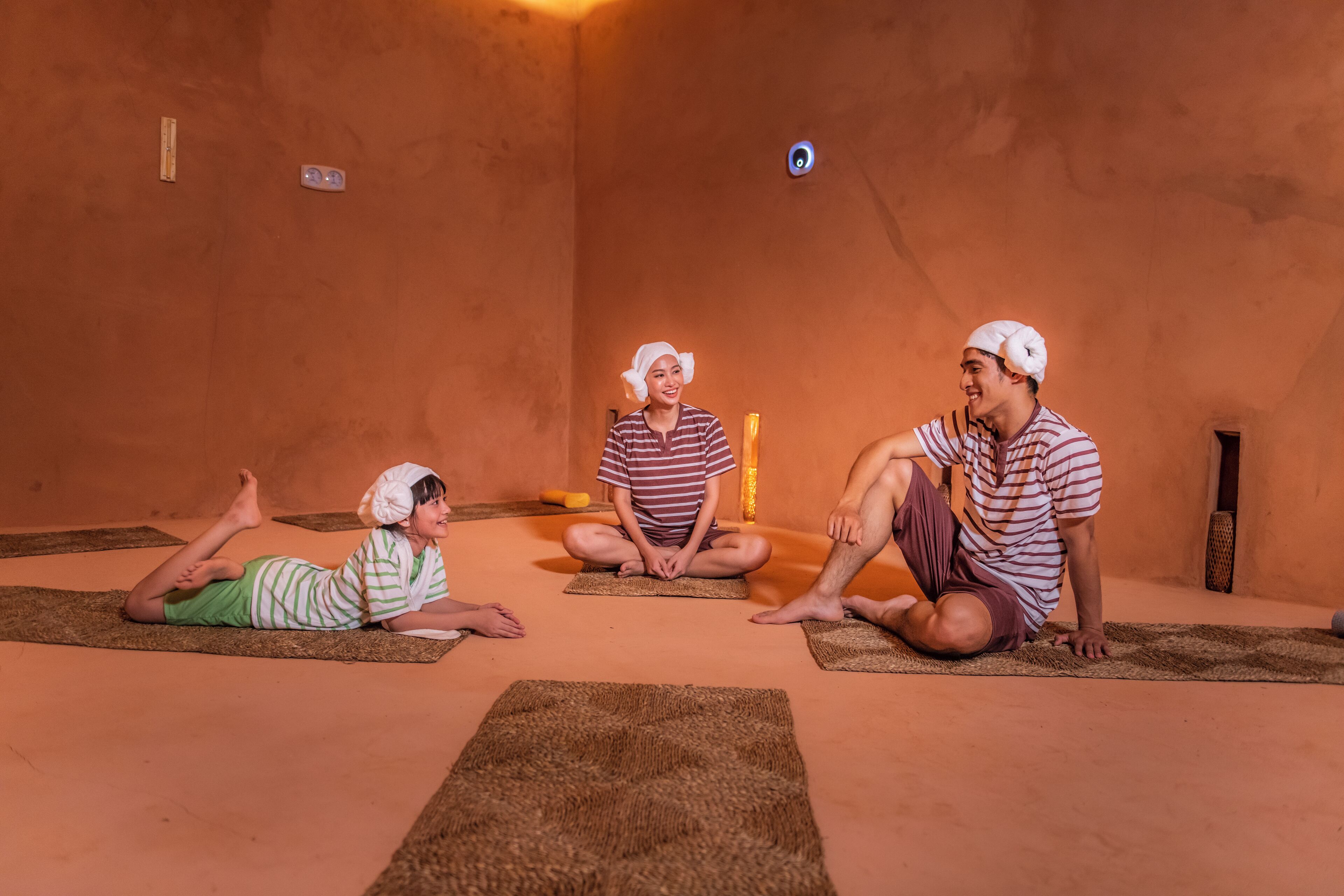 Three people sitting on mats in a room with orange walls and a small window.
