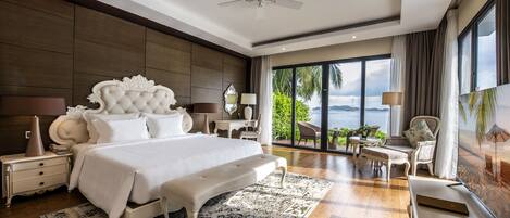 A spacious bedroom with a large bed, a ceiling fan, a view of the outdoors, and a balcony with seating.