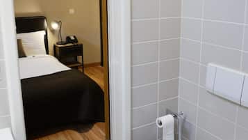 A hotel room with a separate bathroom, a bed with a black headboard, a bedside table with a lamp, and a toilet.