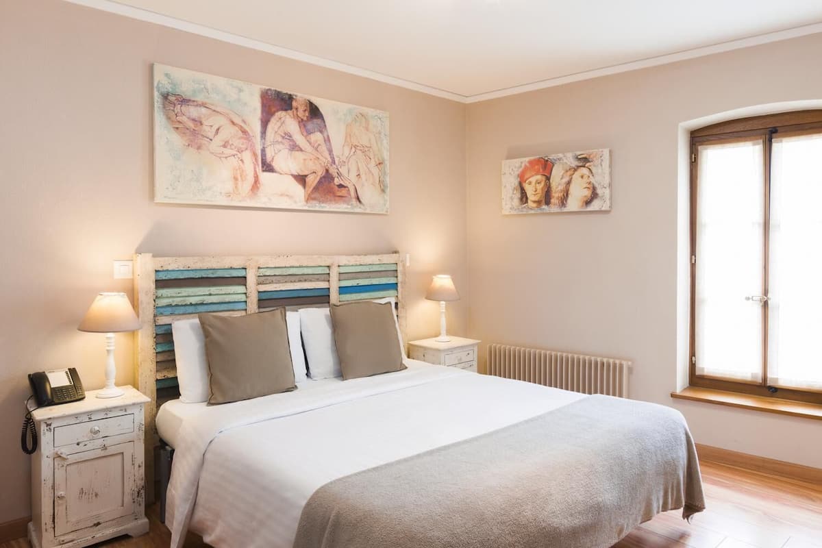 Quarto com uma cama, duas mesas de cabeceira, um radiador e duas pinturas penduradas na parede.