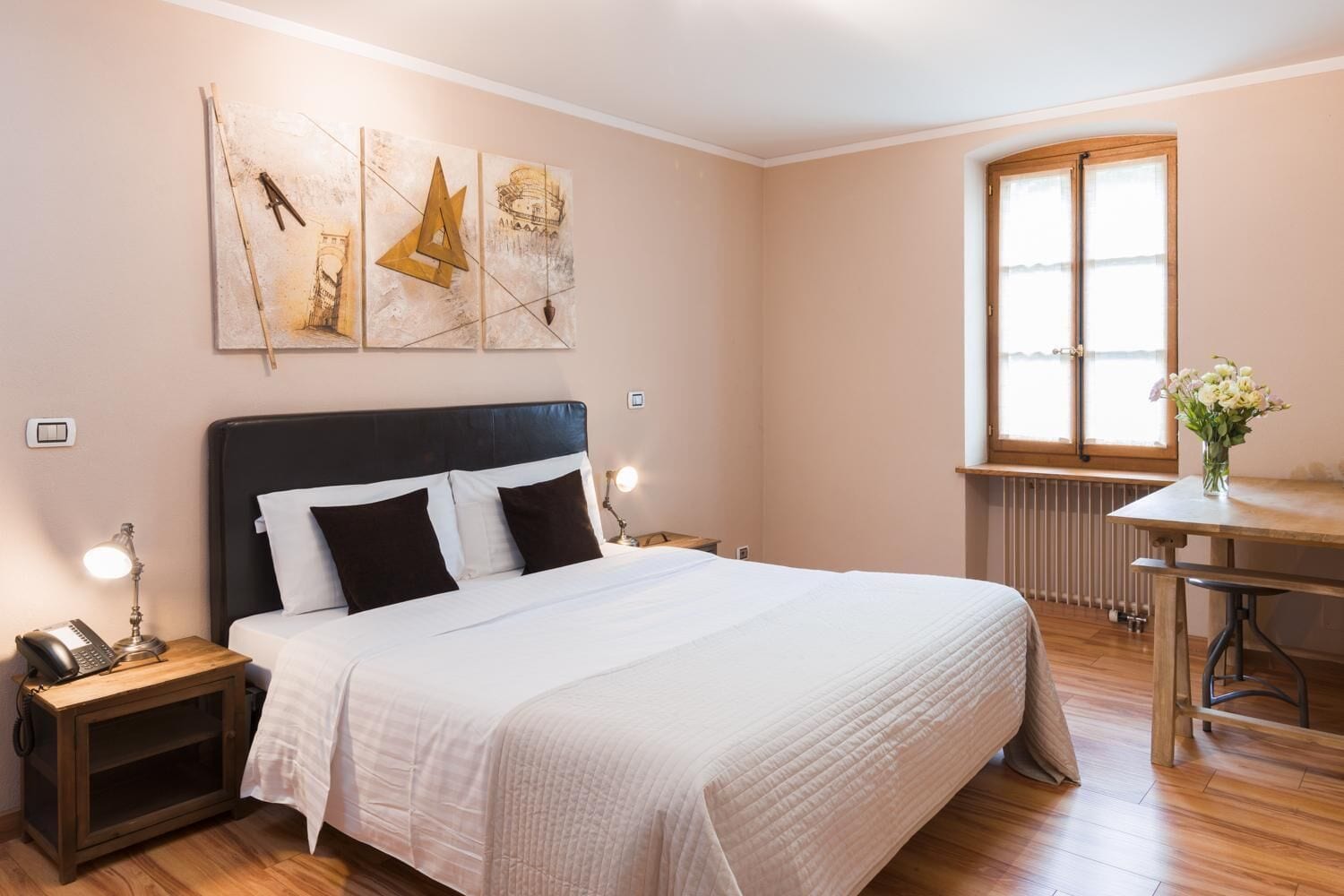 Ein ordentlich eingerichtetes Schlafzimmer mit einem großen Bett, Nachttischen mit Lampen, einem kleinen Tisch mit Blumen und einem Fenster mit Blick.
