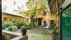 A courtyard with cobblestone paths, potted plants, and a view of buildings in the background. - The Spanish Suite Piazza di Spagna (Rome)