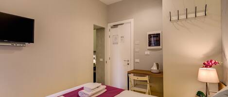 A hotel room with a bed, a flat-screen TV, a desk with a lamp, and a chair.