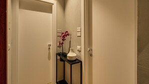 A hallway with a white door, a small black console table with a vase and flowers, and a wall-mounted light switch. - The Spanish Suite Piazza di Spagna (Rome)