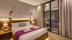 A hotel room with a large bed, a nightstand with a lamp, a potted plant, and a view of the city through a large window. - The Spanish Suite Piazza di Spagna (Rome)