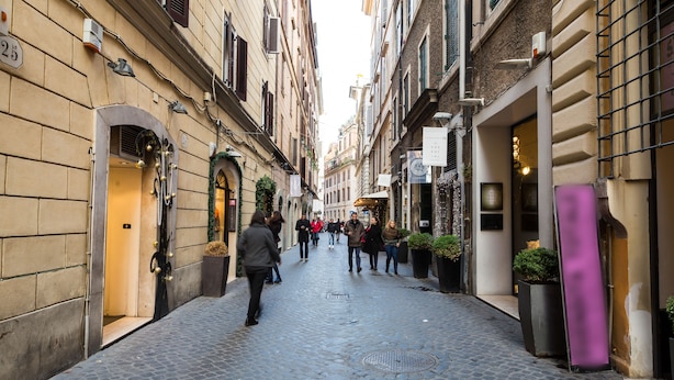 A narrow cobblestone street lined with historic buildings, some with shop fronts and signage. - The Spanish Suite Piazza di Spagna (Rome)