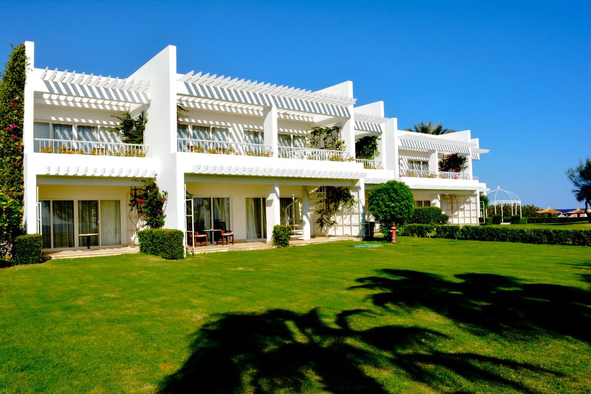 A modern hotel with a white facade, multiple balconies, and a well-maintained lawn.
