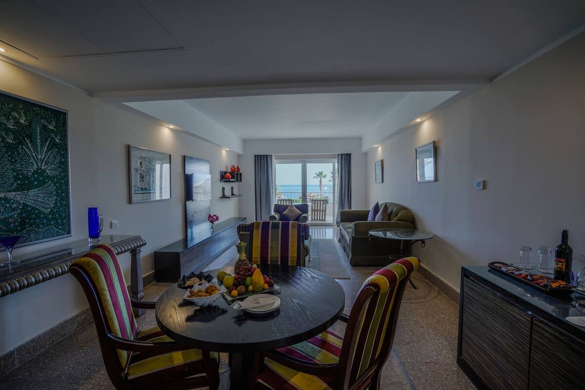 A modern living room with a dining area, a sofa, and a balcony with a view of the sea.