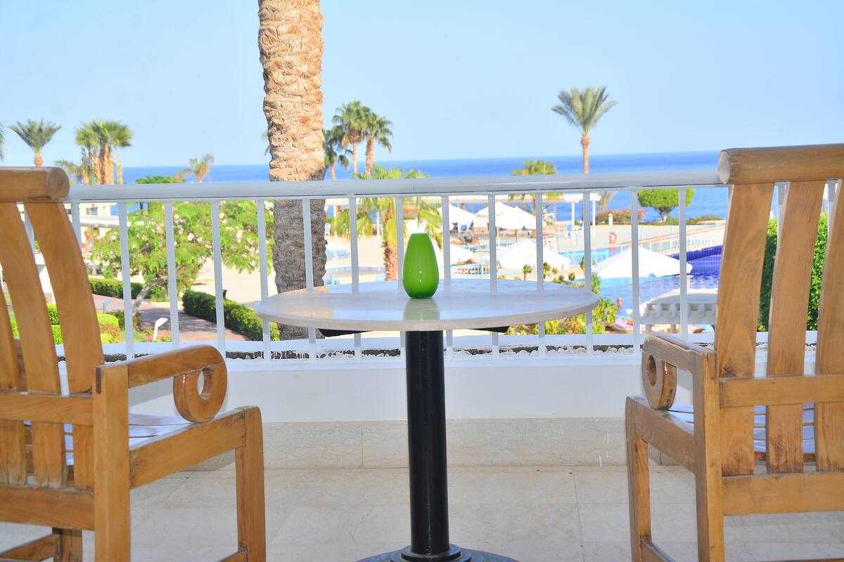 A wooden table with a green vase, two wooden chairs, and a view of the beach and ocean.