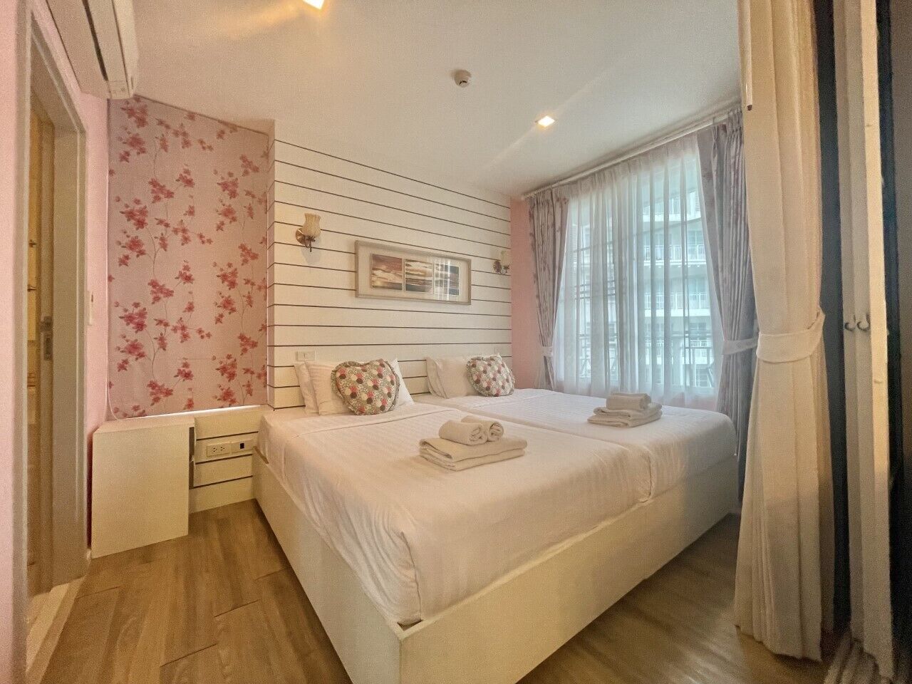 A bedroom with a large bed, two bedside tables, a dresser, and a window with curtains.