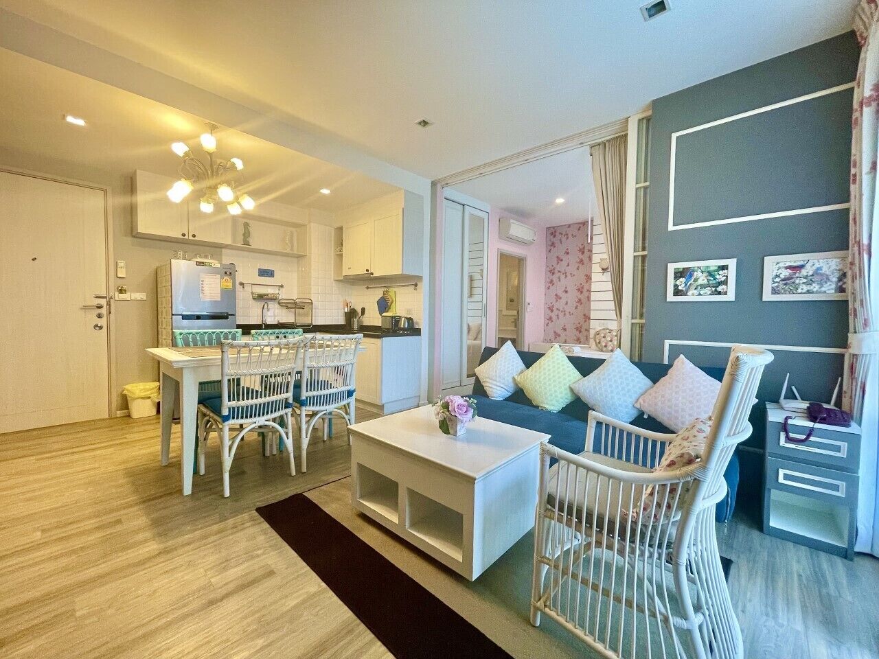Un salon moderne comprenant un coin repas, un canapé blanc agrémenté de coussins colorés, une table basse blanche et un fauteuil en osier blanc.