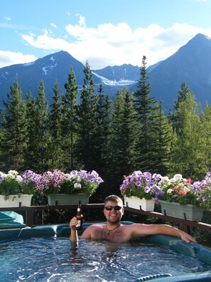 A person in a hot tub with a mountain view, surrounded by potted flowers. - Silvern Lake Trail Bed & Breakfast (Smithers)