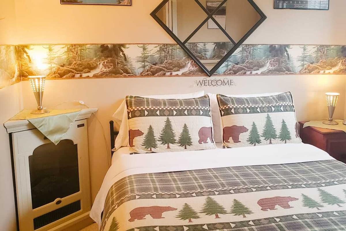 A bed with a forest-themed bedding set, a welcome sign above the bed, and two bedside lamps.