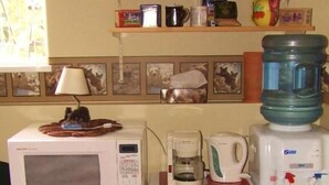 Una kitchenette con microondas, cafetera y dispensador de agua sobre una mesa de madera.