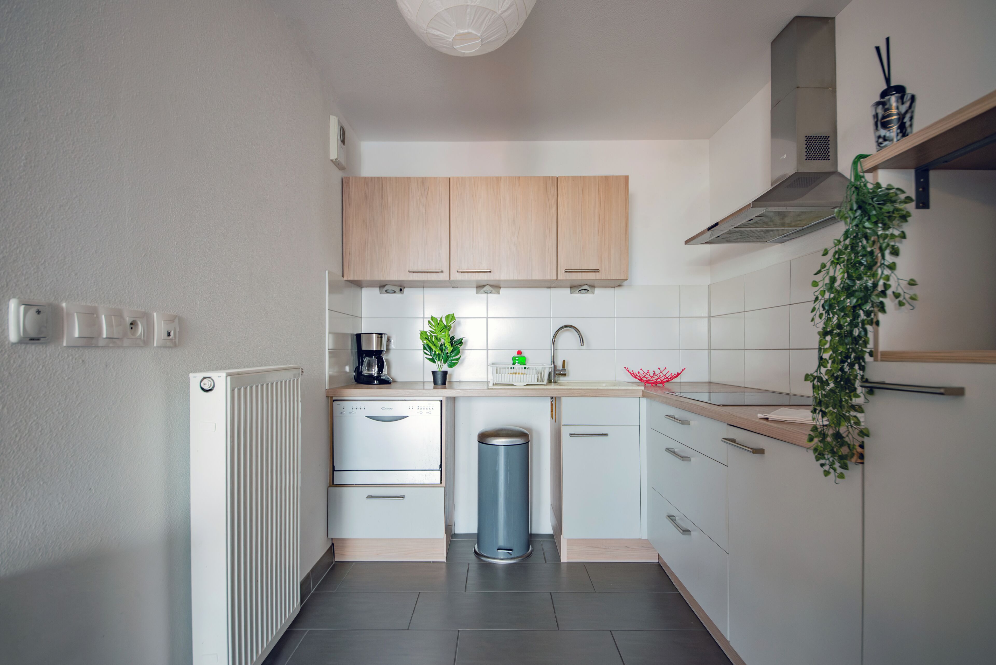 Una cocina moderna con armarios blancos, estufa de acero inoxidable, cafetera y un cubo de basura.