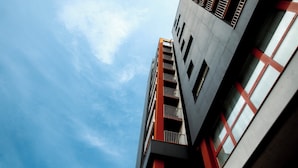A modern building with a prominent red and grey facade, multiple balconies, and large windows. - Appart du Trident (Mulhouse)