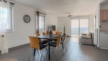 A modern living room with a dining area, a sofa, a TV, and a balcony with a view.