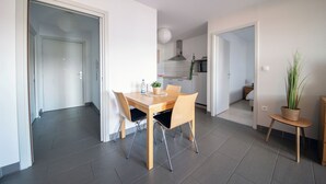 A modern kitchen with white cabinets, a stainless steel range hood, and a dining area with a wooden table and chairs. - Appart du Trident (Mulhouse)