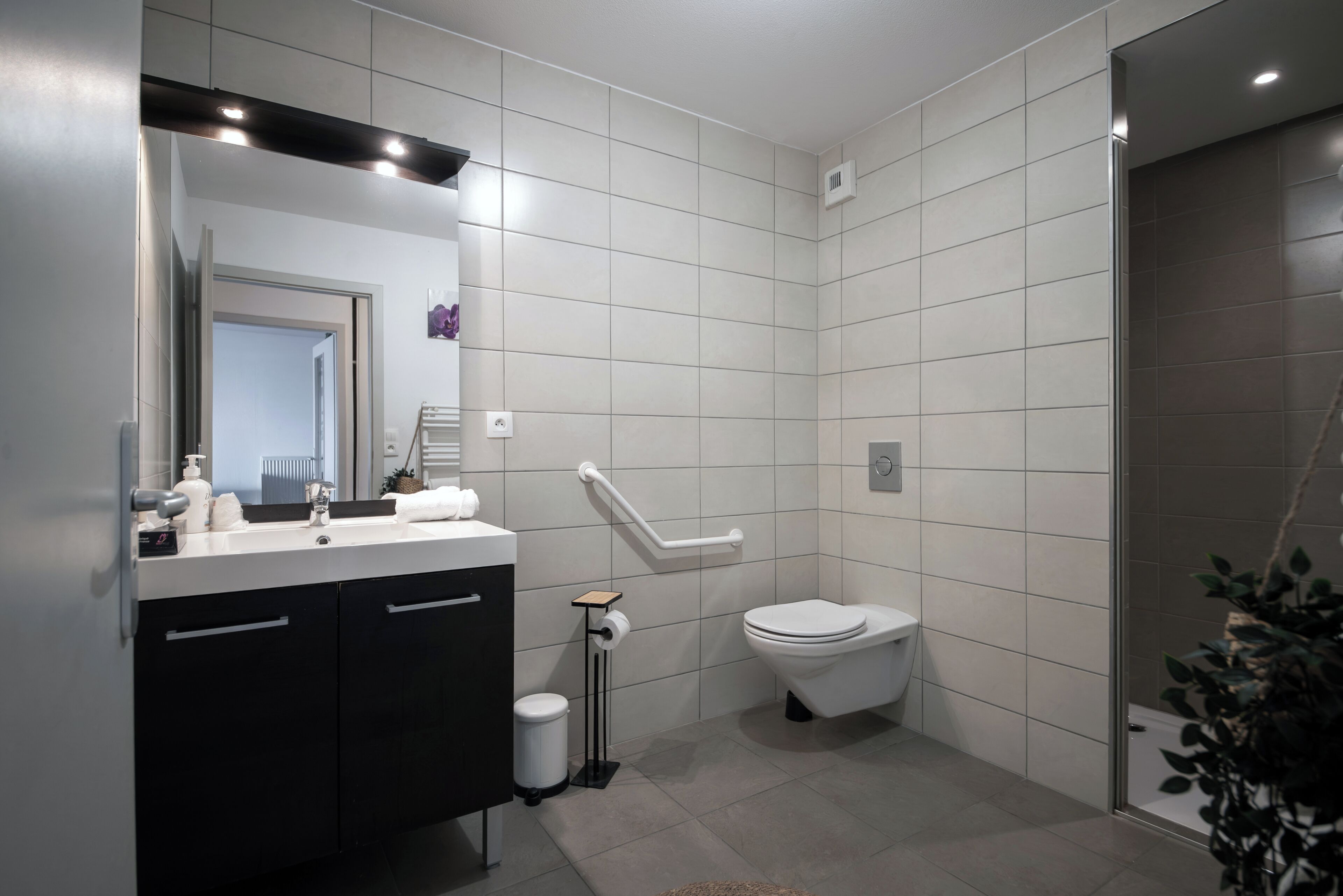 A modern bathroom with a white toilet, a black vanity, a hand dryer, and a small trash bin.