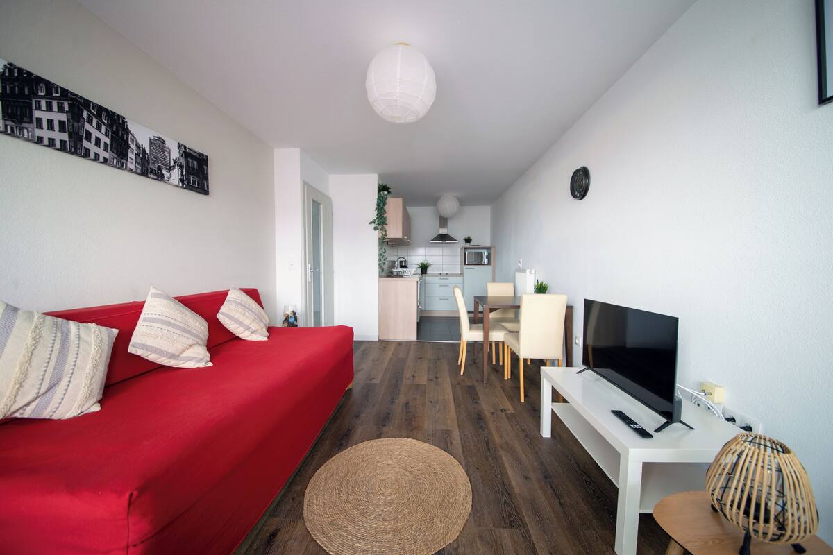 Una sala de estar moderna con un sofá rojo, un televisor y un comedor con una mesa y sillas blancas.
