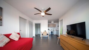 A modern living room with a red sofa, a wooden TV stand, a ceiling fan, and a dining area in the background. - Appart du Trident (Mulhouse)