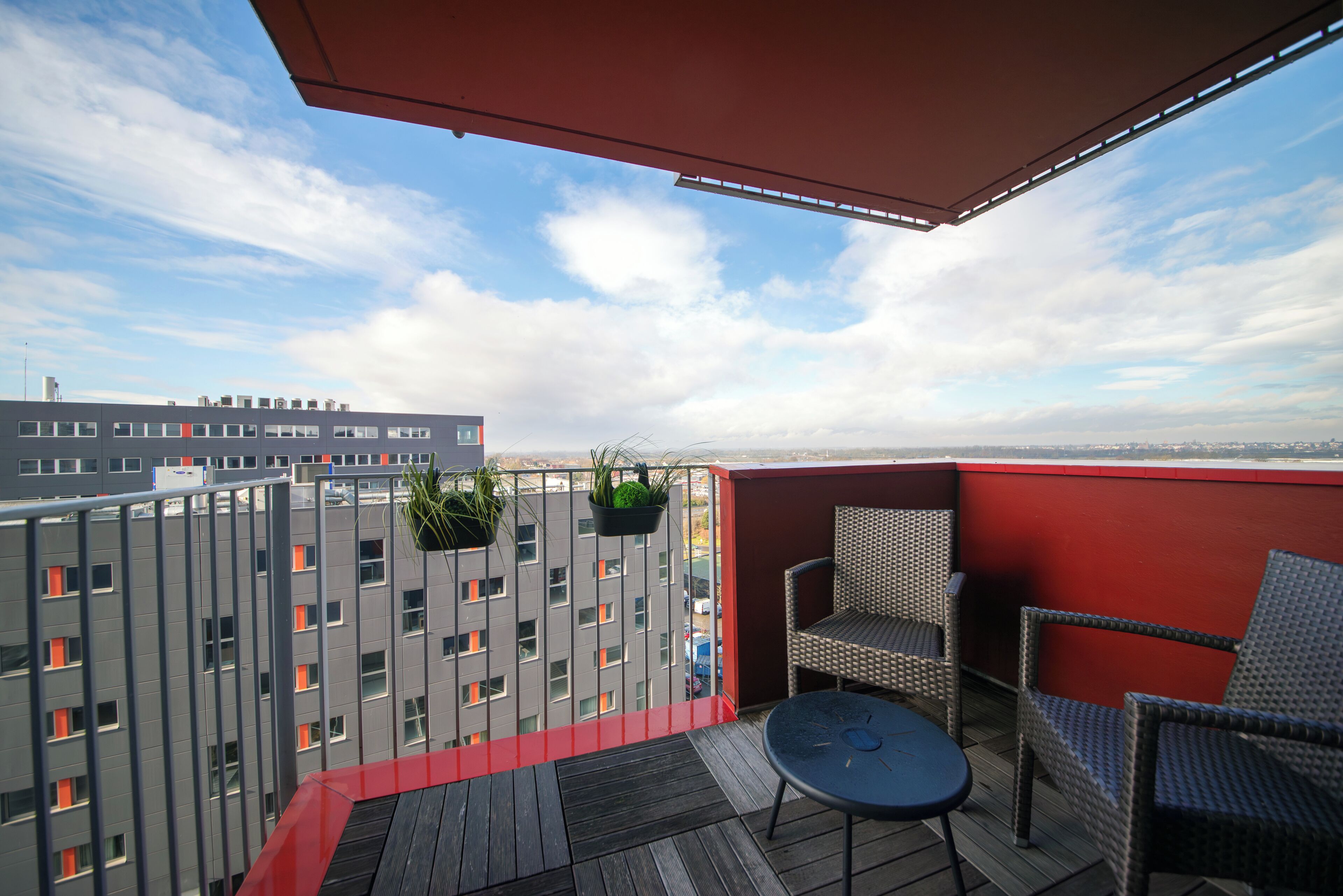 A balcony with wicker chairs, a small round table, and hanging planters.