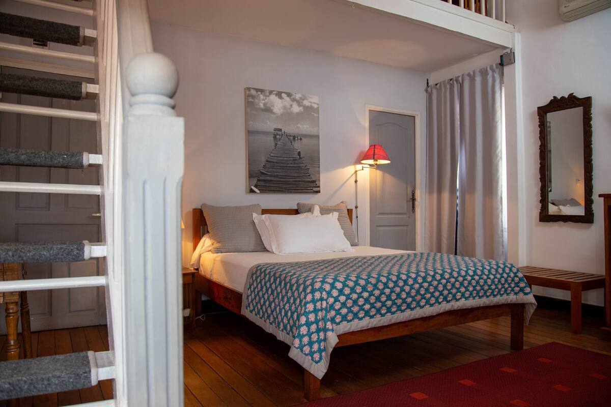 Ein Schlafzimmer mit einem hölzernen Bett, einem Gemälde eines Piers, einer roten Lampe und einem Spiegel an der Wand.