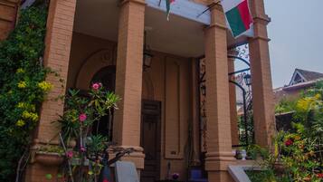 A two-story brick building with a balcony, a flag, and a staircase leading to the entrance.
