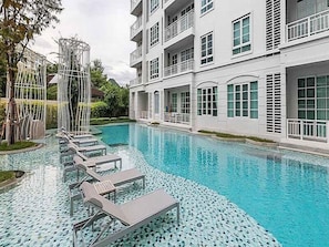 A swimming pool with lounge chairs and a white building with balconies.