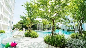 A swimming pool surrounded by lush greenery and a white building with balconies.