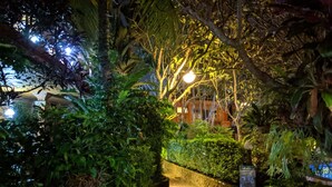 A pathway through a lush garden at night, illuminated by street lamps. - Okawati Hotel (Ubud)