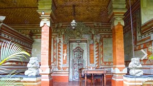A traditional building with a tiled floor, a central door with intricate carvings, and stone lion statues on either side. - Okawati Hotel (Ubud)