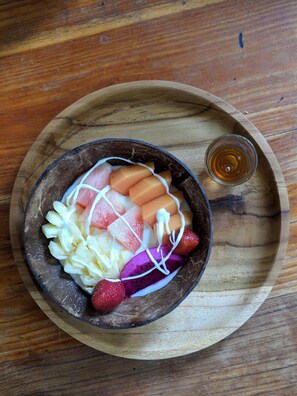 A wooden tray with a bowl containing a fruit salad and a small glass of honey. - Okawati Hotel (Ubud)