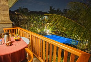 A wooden deck with a pool, surrounded by tropical plants and a night sky. - Okawati Hotel (Ubud)