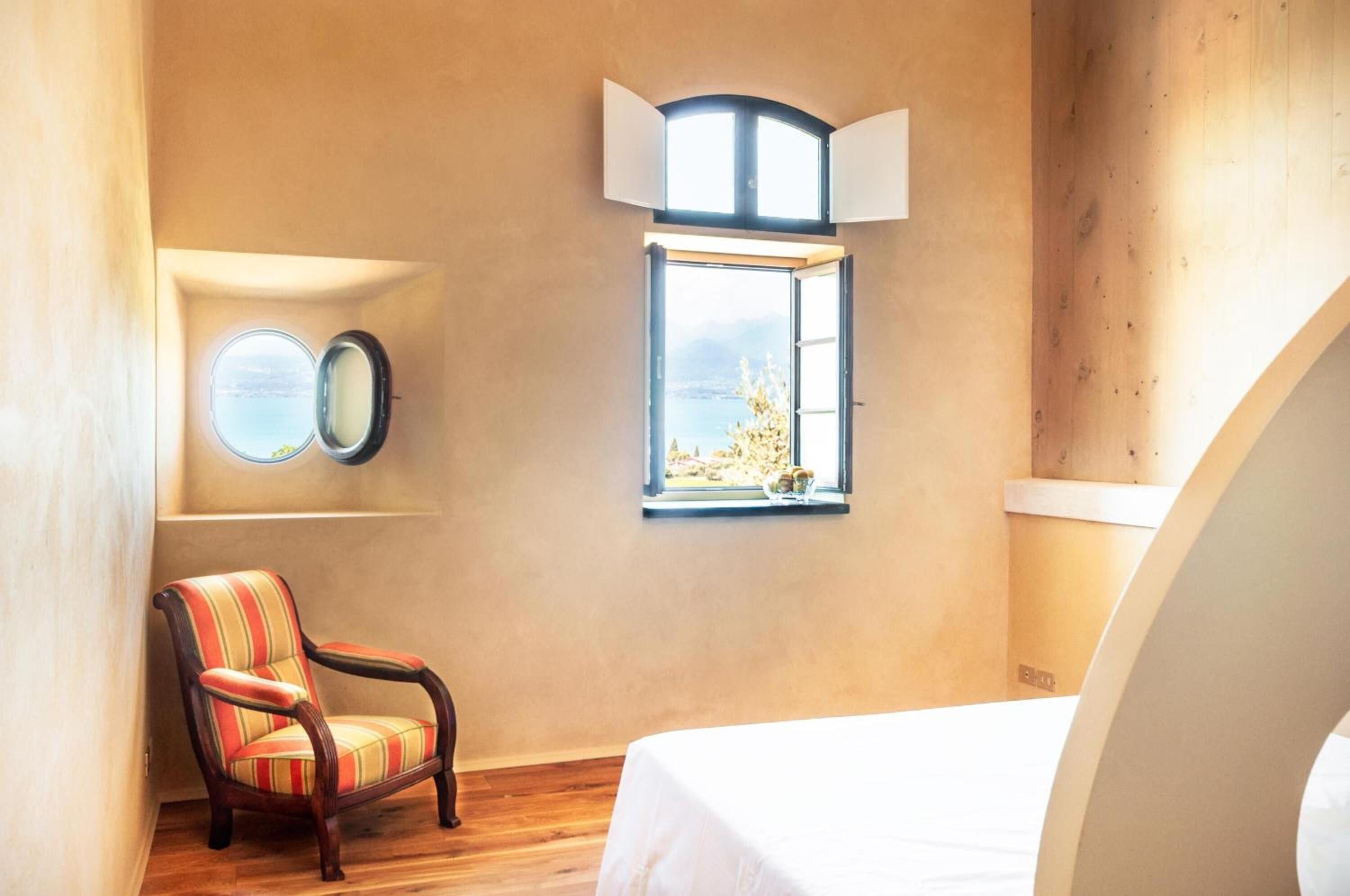 Un dormitorio con una cama grande, una ventana con vistas, una silla y un espejo fijado a la pared.