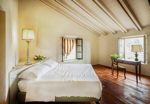 A bedroom with a bed, a desk, and a chair. There is a window with curtains, a lamp, and a plant on the desk.