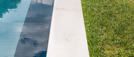 Una piscina con borde blanco y un área verde a su lado.