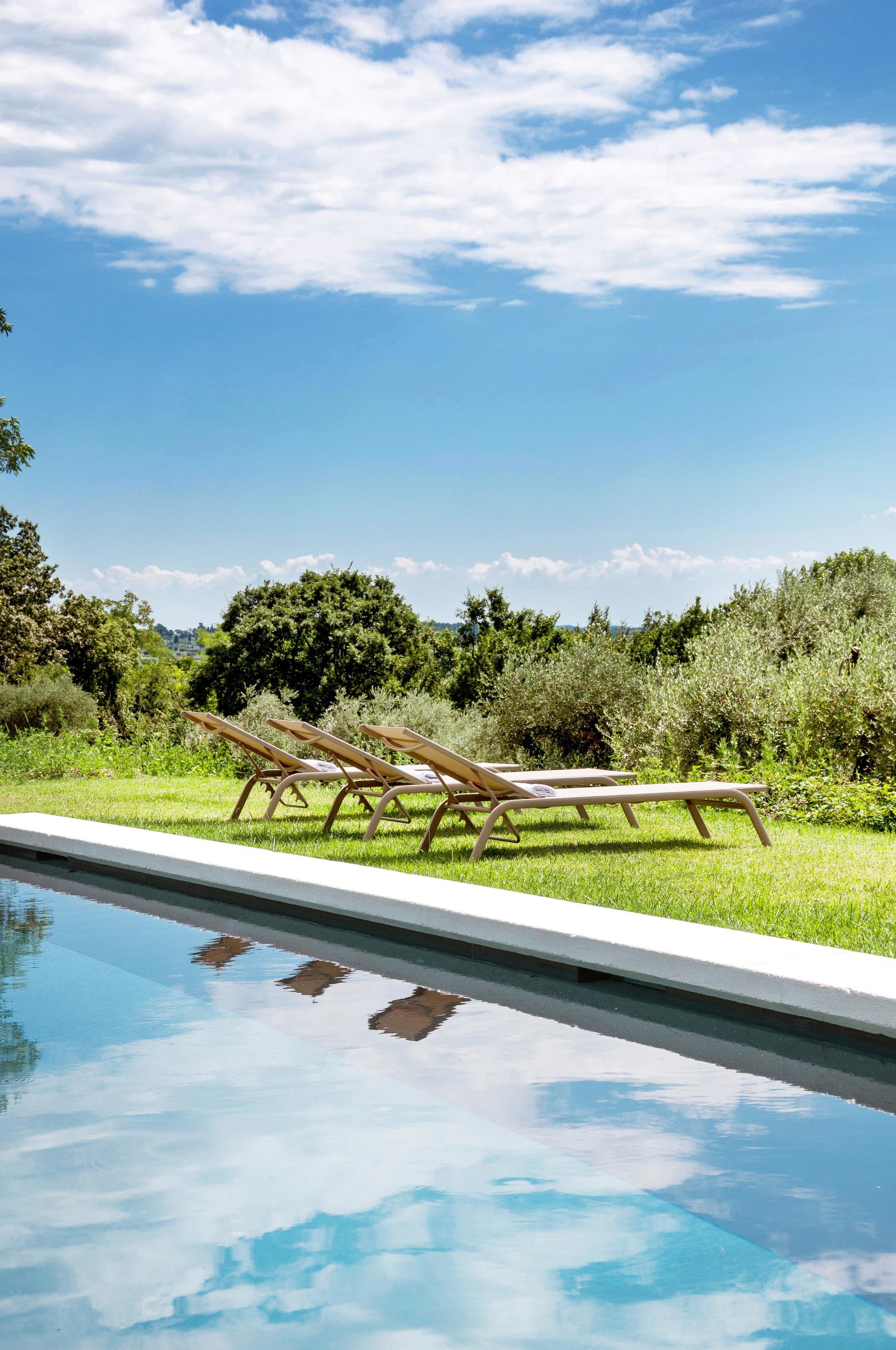 A swimming pool with lounge chairs and a grassy area with trees in the background.