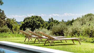 A swimming pool with lounge chairs and a grassy area with trees in the background.