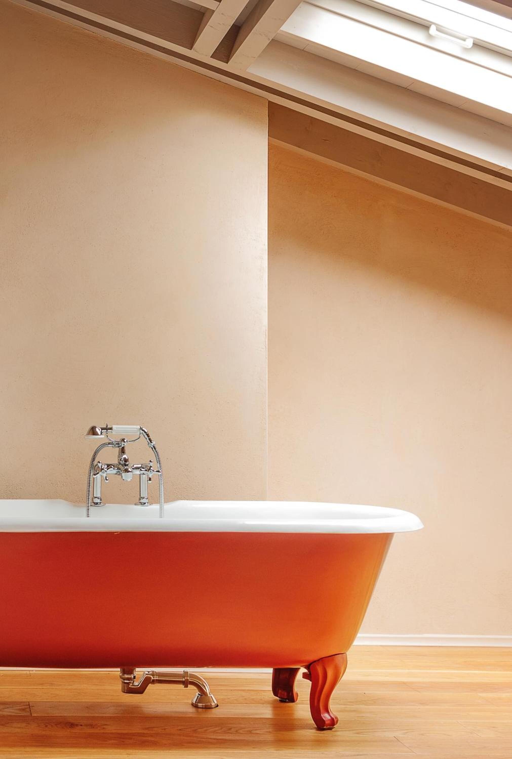 Un baño moderno con una bañera roja de patas de león, un grifo cromado y suelo de madera.