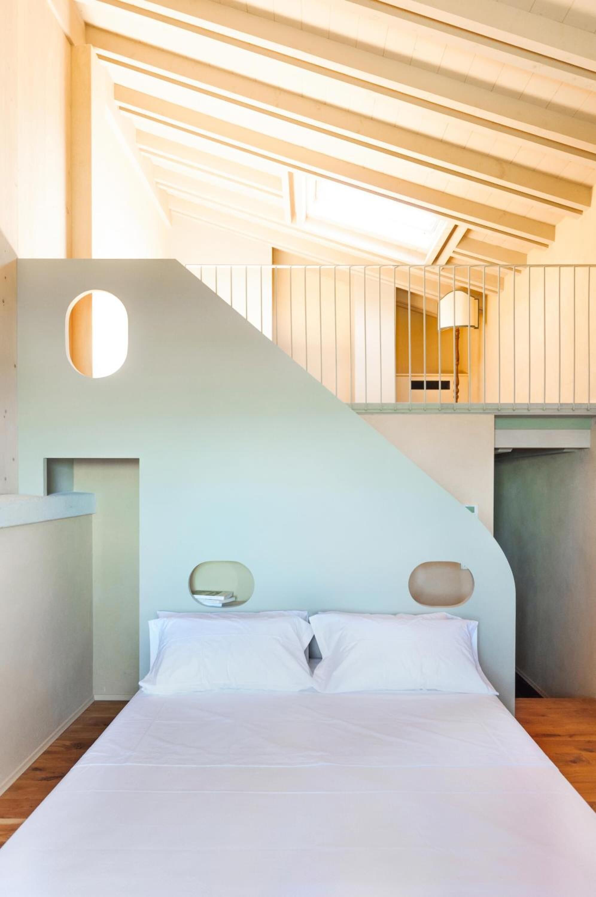 A modern bedroom with a large bed, a staircase, and a circular window.