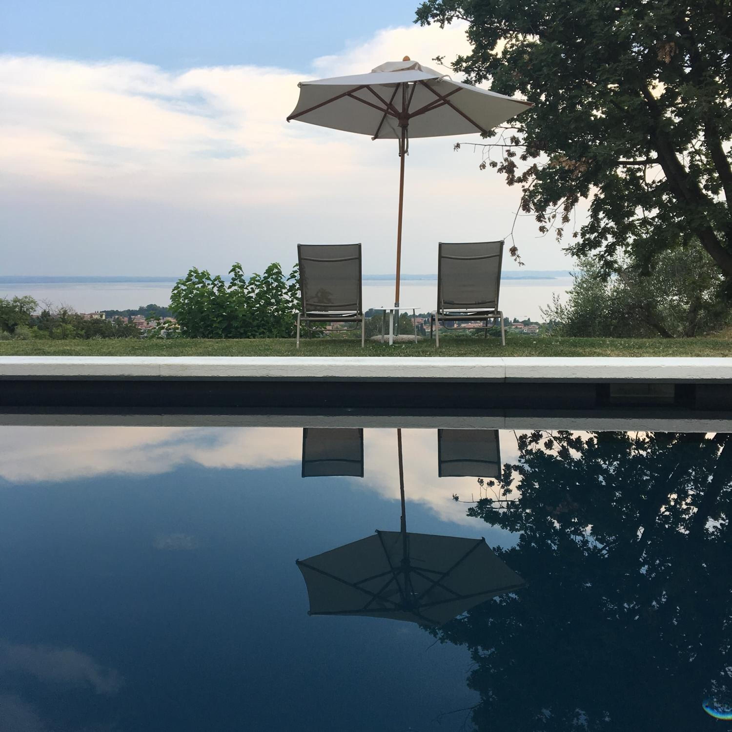 Zwembad met twee stoelen en een parasol, met spiegeling van de lucht en bomen.