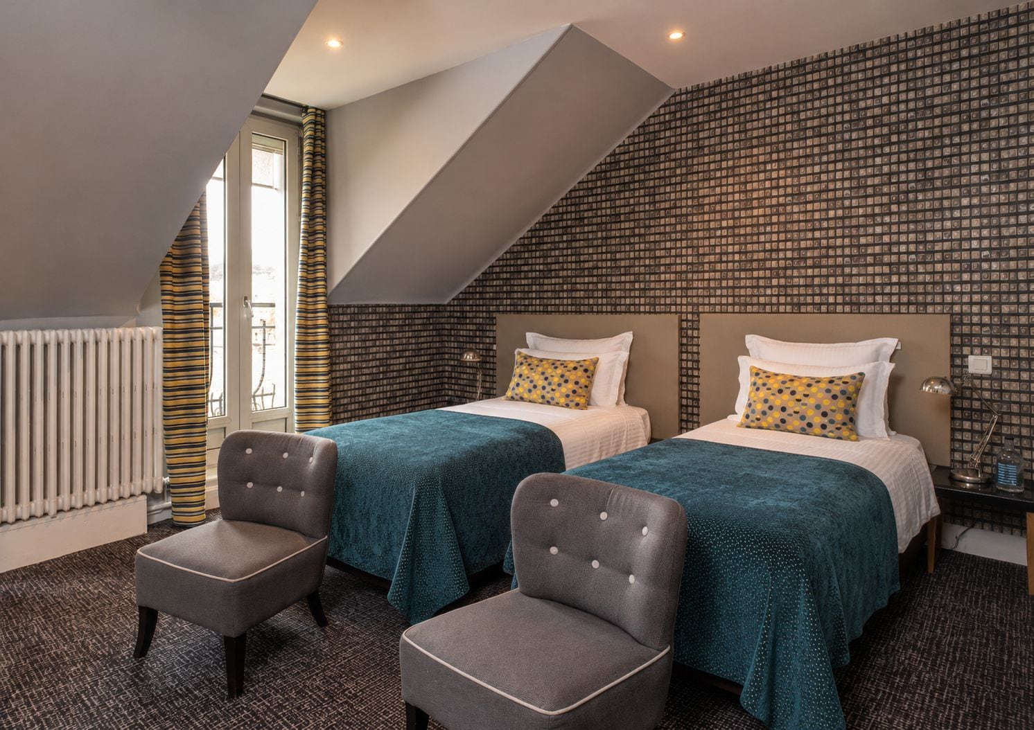 A hotel room with two beds, a radiator, a window with curtains, and a chair.